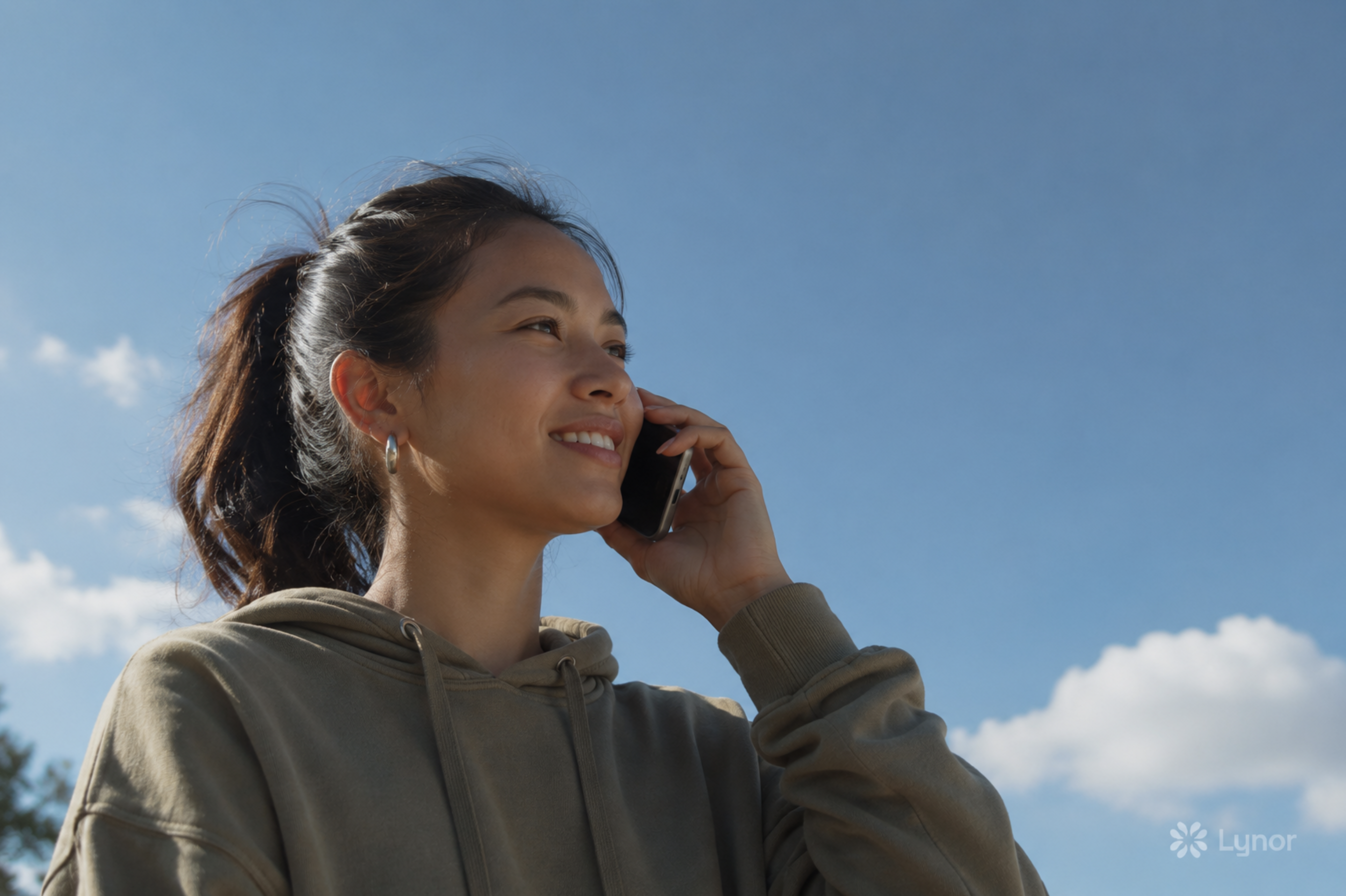 A person speaking on the phone in a bright outdoor scene.